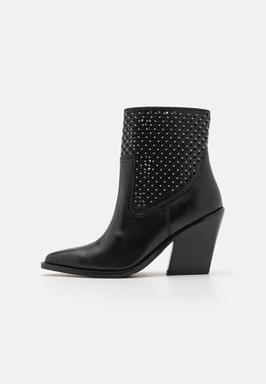 Botte cheville en cuir noir avec bout pointu, talon haut empilé, et dessus orné de petites perforations carrées et de clous.