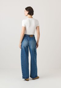 Lengvas baltas trumpomis rankovėmis marškinėliai, derinami su aukštu liemeniu plačiomis mėlynomis džinsinėmis kelnėmis. Kelnės turi rudą odinį ženkliuką gale.