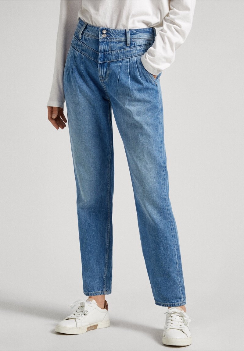 Jeans in denim azzurro chiaro a gamba dritta con dettagli plissettati in vita, due tasche laterali e una texture liscia. Indossati con sneaker bianche.