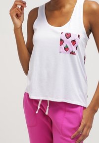 Biała bawełniana tank top z różową kieszenią w truskawkowy wzór. Połączony z luźnymi różowymi spodniami dresowymi. Prosty design i casualowy styl.