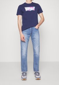 Camiseta de algodón azul marino con el logo colorido de Levi's, combinada con jeans rectos de mezclilla azul claro y zapatillas deportivas grises con acentos.