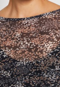 Haut transparent à motifs noirs avec de grandes formes irrégulières dans des tons de marron, gris et pastels doux, doté d'un large décolleté.