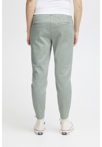 Mátově zelené kostkované kalhoty se slim fit, se dvěma zadními kapsami a manžetami na kotnících, v kombinaci s béžovými vysokými teniskami.