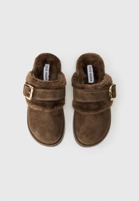 Clog din suede maro, cu blăniță pufoasă la interior și bretele ajustabile, având catarame aurii, etichetate cu Steve Madden.