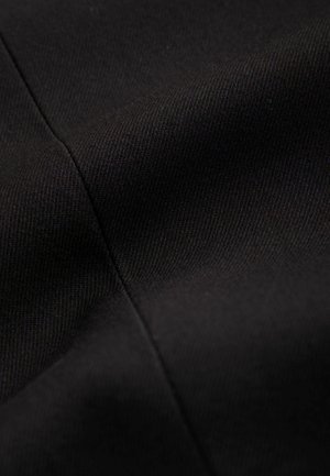 Primer plano de tela negra con textura de tejido diagonal visible y una costura cosida que corre verticalmente.