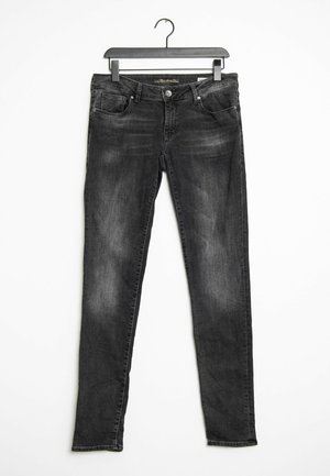 Sorte, falmede skinny jeans hængende på en sort plastikbøjle mod hvid baggrund.