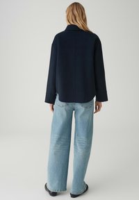 Giacca oversize blu marina scuro con colletto, abbinata a jeans a gamba larga azzurri. Tessuto liscio e design semplice senza decorazioni.