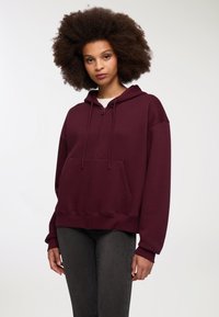 Felpa zip-up bordeaux con tasca a marsupio, cappuccio con coulisse e vestibilità comoda. Presenta polsini e orlo a costine, realizzata in tessuto morbido.