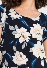 Módní blůza s krátkým rukávem v námořnické modři, zdobená velkými krémovými a růžovými květinami s zelenými listy. Kulatý výstřih a volný střih.