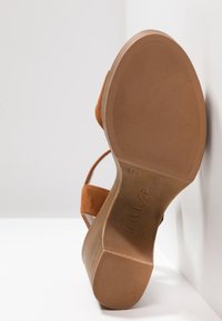 Sandale compensée en daim beige avec semelle en caoutchouc, motif de la bande de roulement visible, et nom de la marque "Unisa" embossé sur le dessous.