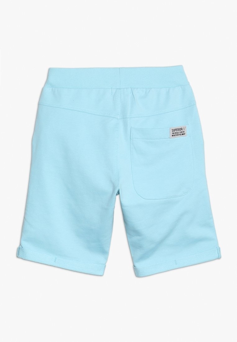 Shorts bleu clair pour tout-petit avec une taille élastique, une poche plaquée à l'arrière et une petite étiquette portant l'inscription « SUPERIOR// tu peux vraiment faire ce que tu veux. »