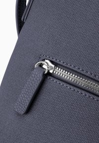 Primo piano di una borsa di tessuto navy con una cerniera argento e un tira-zip in pelle navy abbinato.