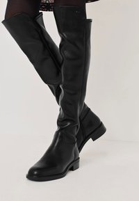 Lange schwarze Lederstiefel mit einem eleganten Design, flachem Absatz und Nähdetails. Das Material hat eine glatte Textur und eine taillierte Silhouette.