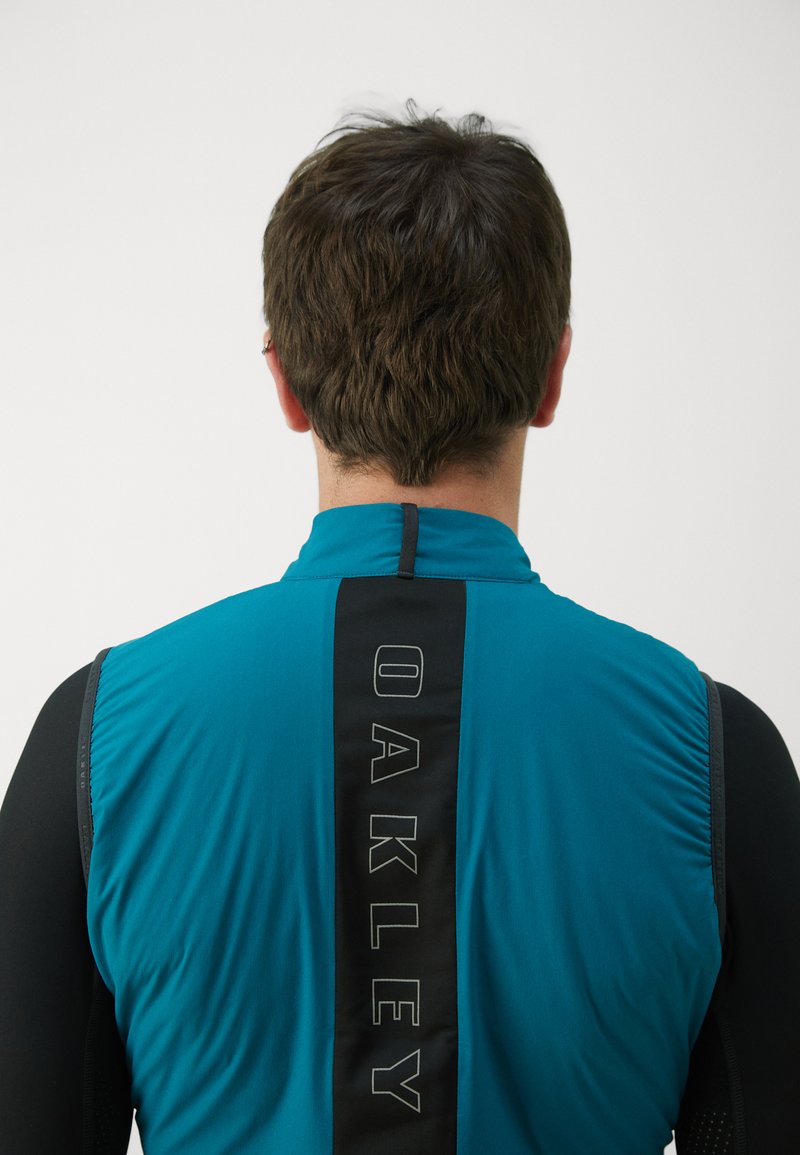 Herren Sportjacke in Teal und Schwarz, mit hohem Kragen, Reißverschluss und einem vertikalen Logodesign auf dem Rücken.