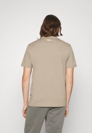 Mann mit mittellangen braunen Haaren, der von hinten zu sehen ist und ein beiges T-Shirt mit kurzen Ärmeln trägt, auf dessen oberem Rücken "BOSS" gedruckt ist.