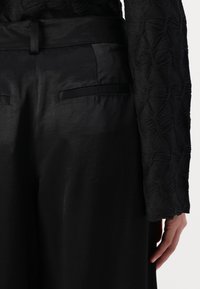 Top nero testurizzato con motivo tridimensionale, abbinato a pantaloni neri lisci a vita alta con tasche laterali e una cintura.