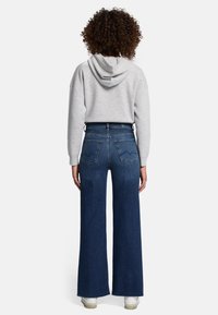 Jeans a zampa d'elefante in denim con vita alta, colore blu scuro, gambe larghe e dettagli di cucitura sulle tasche posteriori. Abbinati a un felpa con cappuccio grigia.