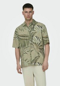 Korte mouw shirt in beige met een groot groen tropisch bladerenprint. Voorzien van een knoopsluiting aan de voorkant en een borstzak. Gladde, lichte stof.