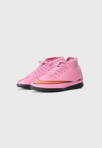Et par rosa innendørs fotballsko med svarte såler og oransje Nike-svømmere, mid-top stil, og lisser knyttet i sløyfer.