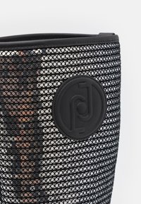 Bottine en maille noire avec un motif texturé, des accents brillants et un badge logo circulaire. Le design est épuré avec une silhouette moderne.