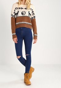 Knit sweater with a cream and brown color block design, featuring black animal motifs. Paired with blue ripped skinny jeans and tan boots.