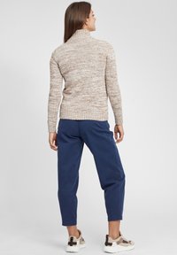 Strik turtleneck sweater i beige og brun meleret mønster, parret med marineblå tapered bukser og sneakers med beige accenter.