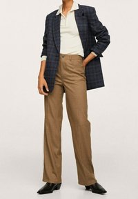 Marynarka w kratę w kolorze granatowym i zielonym, biała bluzka z prążkowanej dzianiny, brązowe spodnie z wysokim stanem oraz czarne, szpiczaste botki, tworzące zorganizowaną sylwetkę.