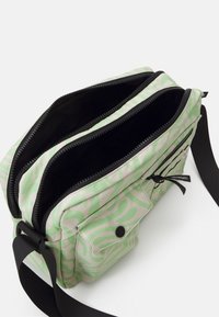 Grön och beige mönstrad väska med två zippered fack, justerbar rem och framficka med tryckknappsstängning.