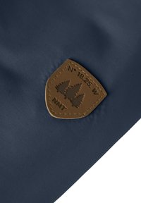 Tissu bleu marine avec un patch en cuir marron présentant trois silhouettes d'arbres, un texte en relief "N° 18.25 W NMT" et des bords cousus.