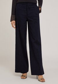 Navyblauwe wijde broek met verticale witte streepjes, voorzien van een knoopsluiting, zijzakken en een gladde textuur.