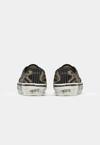 Black and brown leopard print sneakers with a low profile, white rubber sole, and black stitching details on the heel. Prominent logo on the back.