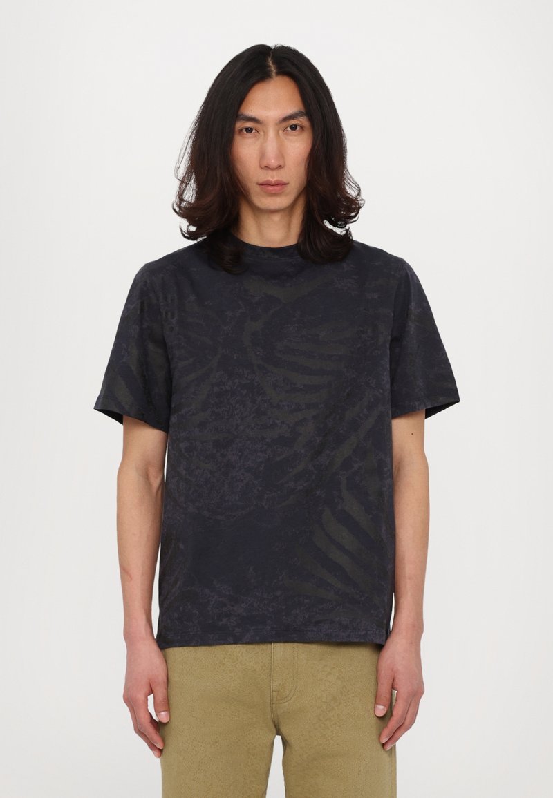 Tricou negru cu mânecă scurtă, cu un model texturat, guler rotund și croială relaxată, asortat cu pantaloni texturați de un bej deschis.