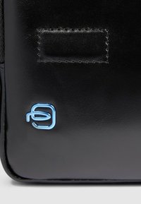 Borsa in pelle nera con una texture liscia, un logo blu prominente e dettagli cuciti. Design compatto con angoli arrotondati.