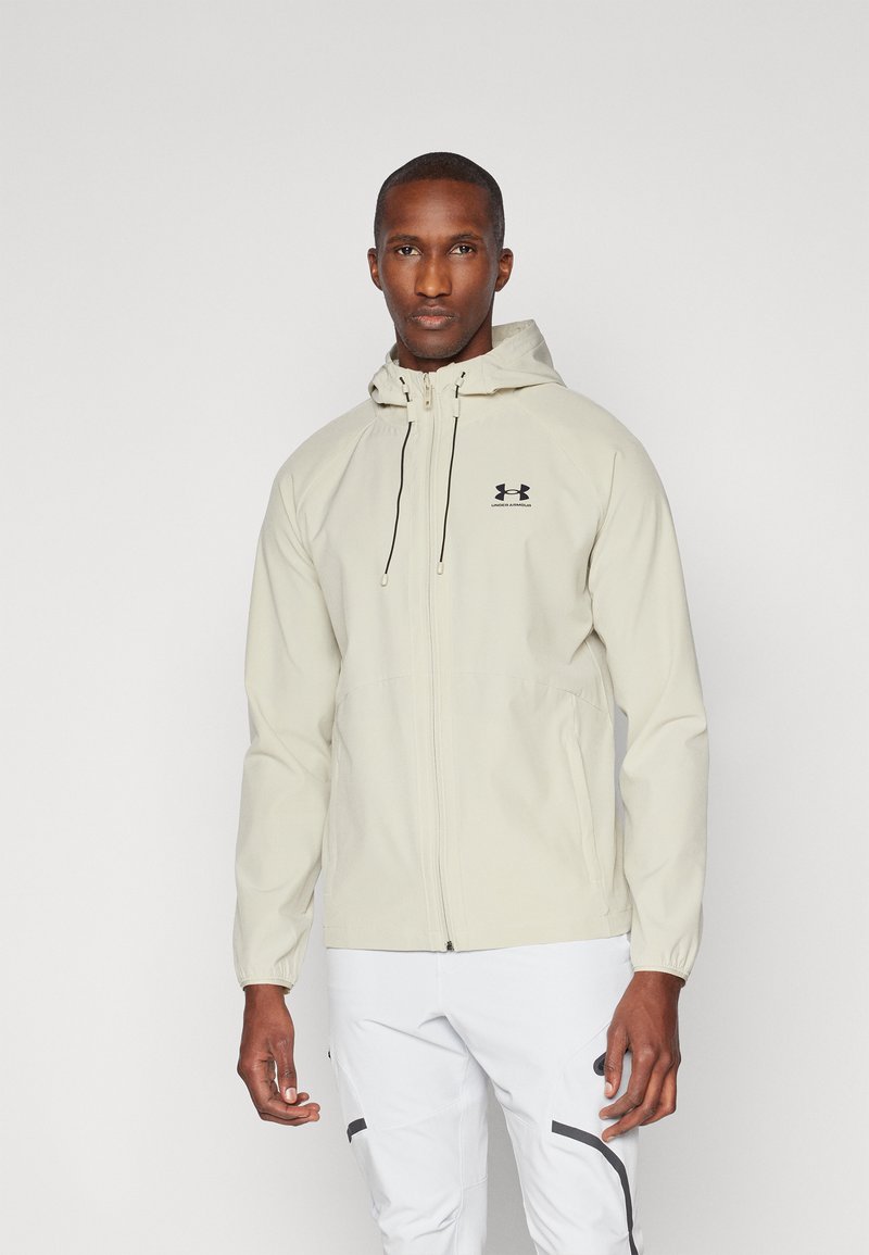 Giacca a zip beige chiaro con cappuccio, dotata di polsini elasticizzati e di un logo sul petto, realizzata in materiale liscio e resistente alle intemperie.