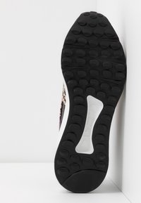 Suola in gomma nera con battistrada circolare e una sezione centrale bianca, parte di una sneaker posizionata verticalmente contro uno sfondo bianco angolare.