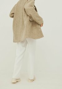 Beige oversize kabát z vlněné směsi, jemná textura, dlouhý silueta; v kombinaci s bílými upravenými kalhotami a krémovými chunky teniskami, minimalistický design.