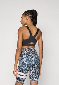 Svart sports BH med utskåret rygg; mønstrete sykkelshorts i mørkeblått og hvitt med rosa horisontale striper; strukturert, tettsittende design.