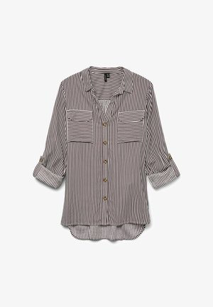 Josla kreklā ar svītrām tumši sarkanā un baltā krāsā, kam ir divas krūšu kabatas, sarullētas piedurknes un izliektu apakšmalu ar nedaudz garāku aizmuguri.