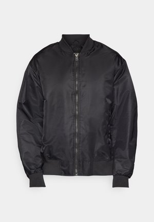 Must beež bomber-jakk, mis on valmistatud siledast ja kergest kangast. Omab esist zipperit, soonikkoe mansette ja püsti kraed. Minimalistlik disain.