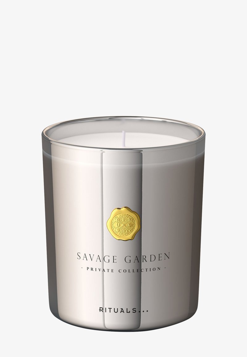 Sølvglasslysestake med hvit voksinnside, dekorert med et gullsymbol og 'Savage Garden'-etikett. Glatt tekstur, sylinderformet.