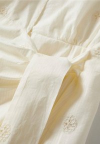 Tela color crema con sutiles rayas verticales, con detalles de bordado floral. Textura suave con detalles de diseño plisado.