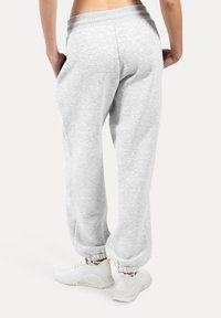 Graue Fleece-Jogginghosen mit elastischem Bund und Bündchen. Der Stoff hat eine weiche Textur. Kombiniert mit weißen Sport Schuhen.
