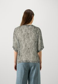 Czarna i biała koszula w wzory z luźnym krojem, krótki rękaw i okrągły dekolt, w połączeniu z jasnoniebieskimi spodniami typu wide-leg.