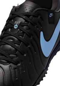 Svart lær atletisk sko med en lys blå Nike swoosh. Har teksturert overflate og svarte snørebånd. Designet for grep og komfort.