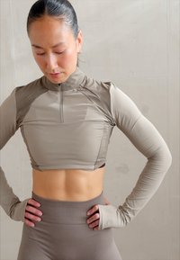 Lys brun avskåret langermet topp med høy krage, med glidelås, teksturerte detaljer og en tettsittende design, kombinert med ribbede høye leggings.