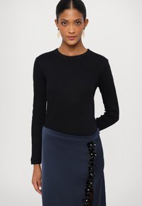 Melnas garās piedurkņu topiņas, kas kombinētas ar zilu svārku, kuram pa sāna šuvi ir ziedu spīdumu akcents. Gluda tekstūra un pieguļošs dizains.