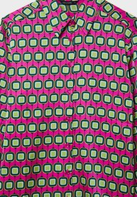 Blusa colorata con un motivo geometrico di quadrati verdi e blu contornati di bianco, su uno sfondo rosa e con bottoni.