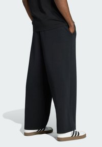 Loose-fitting, black cotton pants with side pockets, featuring a smooth texture. Paired with white sneakers having black stripes.