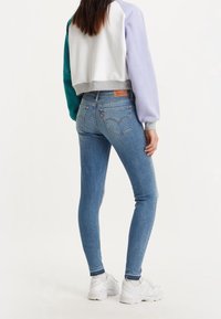 Smala blå jeans med mid-rise midja, med bakfickor och en brun läderlogotyp. Kombineras med en cropped tröja i flera färger.