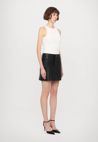 Gonna nera in pelle con dettaglio di lacci davanti, abbinata a un top bianco senza maniche e scarpe con tacco alto nere. Tessuto liscio, design attillato.